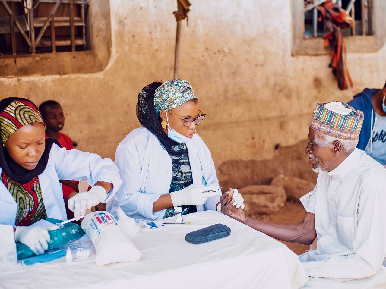 hero-img-02 Healthcare workers assisting elderly man during community outreach in Kaduna, Nigeria.
