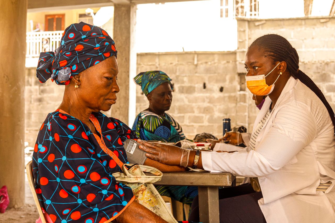 hero-img-01 A healthcare worker checks blood pressure of an elderly woman in a rural clinic setting.
